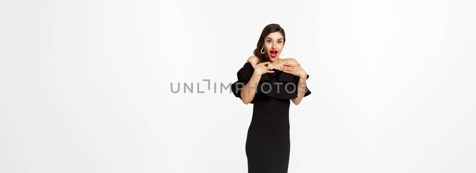 Full length view of woman in elegant dress and red lips, looking surprised, receive gifts on christmas holidays, standing with presents over white background.