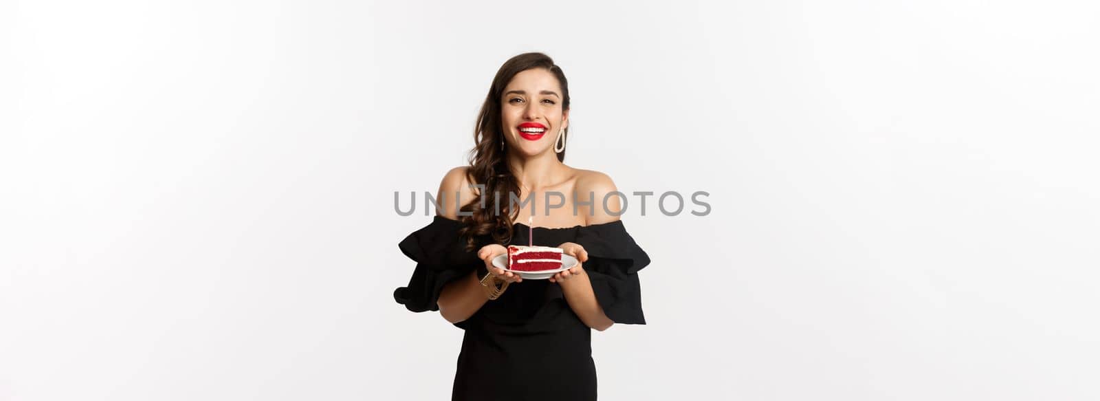 Celebration and party concept. Happy gorgeous woman having birthday, holding b-day cake and smiling, making wish, standing in black dress with makeup by Benzoix