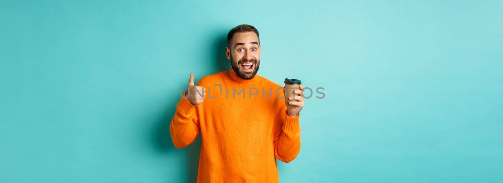 Handsome satisfied man showing thumbs-up, like coffee, smiling pleased, standing over turquoise background by Benzoix