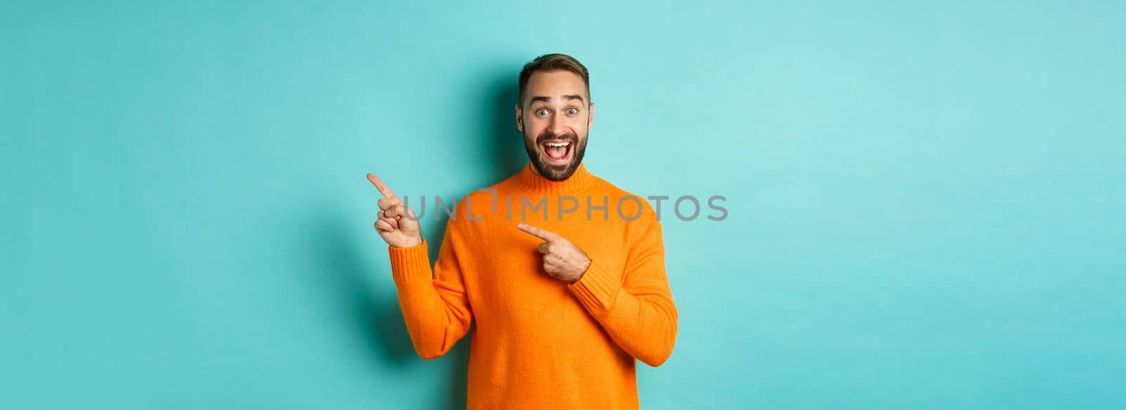 Excited man making an announcement, pointing fingers right your logo, standing over turquoise background.