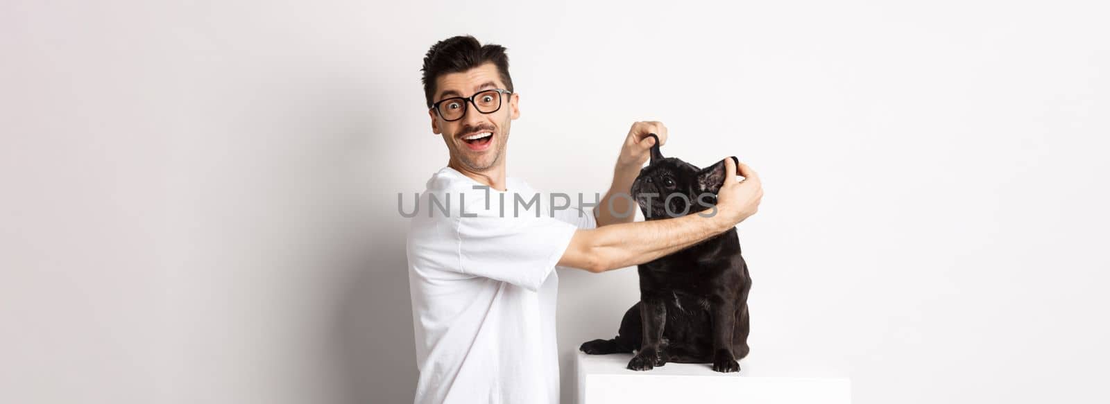 Happy young man looking at camera, showing cute dog ears and feeling rejoice, adopting a pet, standing over white background by Benzoix