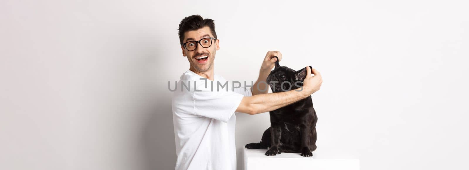 Happy young man looking at camera, showing cute dog ears and feeling rejoice, adopting a pet, standing over white background.