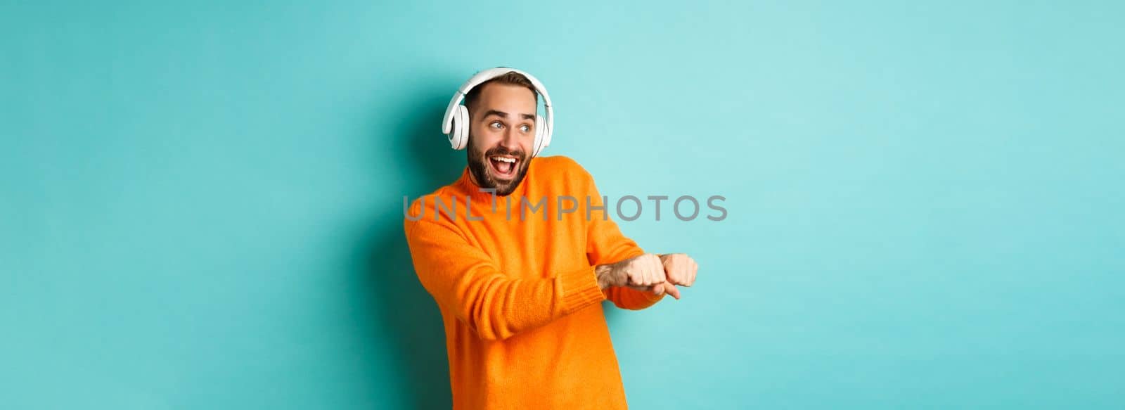 Happy man listening music in headphones and dancing funny, standing over turquoise background by Benzoix