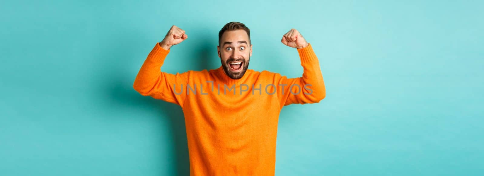 Handsome man celebrating victory, winning and looking happy, triumphing over win, standing over light blue background by Benzoix