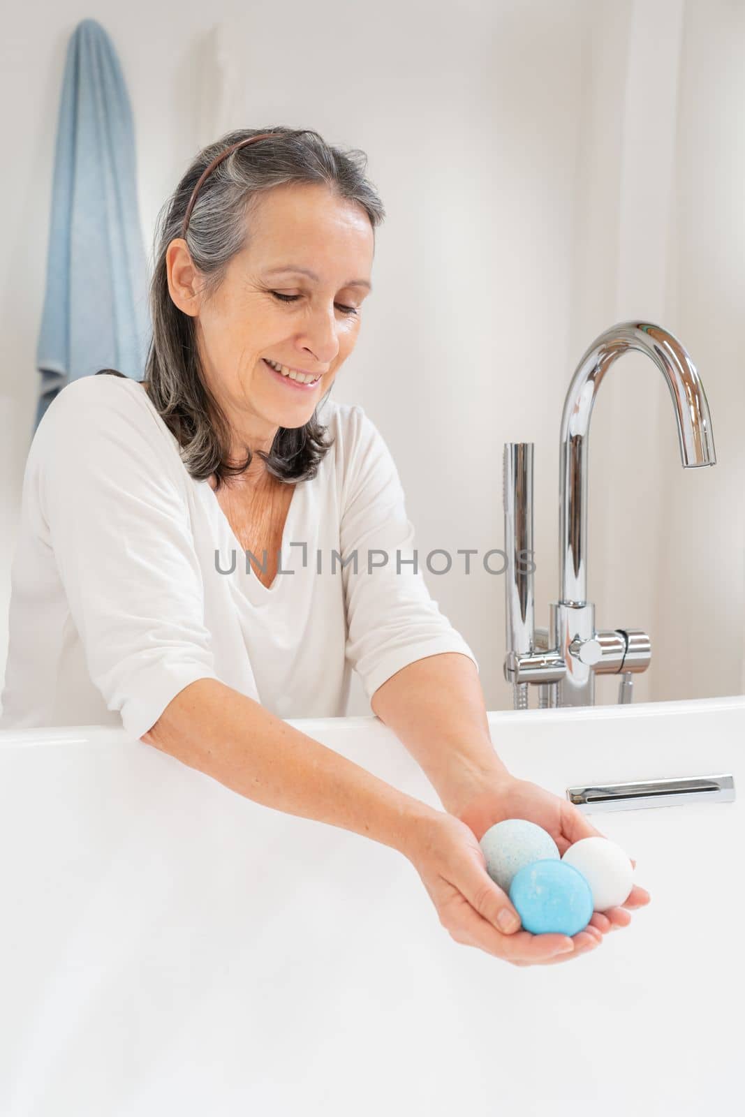 Vertical shot of a happy smiling attractive senior woman morning routine with salt soap aroma balls at luxury bathtub. Body care spa procedures recreation skin care, cosmetic and beauty concept.