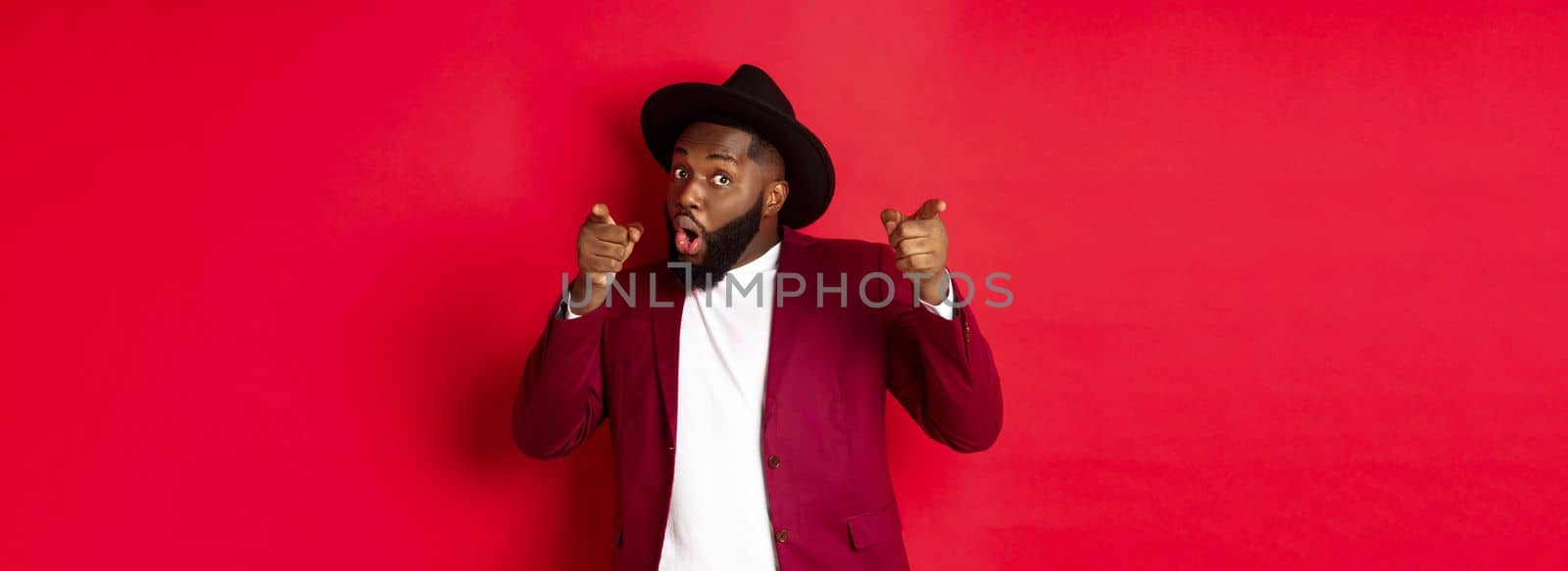 Christmas and people concept. Happy Black man celebrating New Year and dancing, wearing party outfit, red background by Benzoix