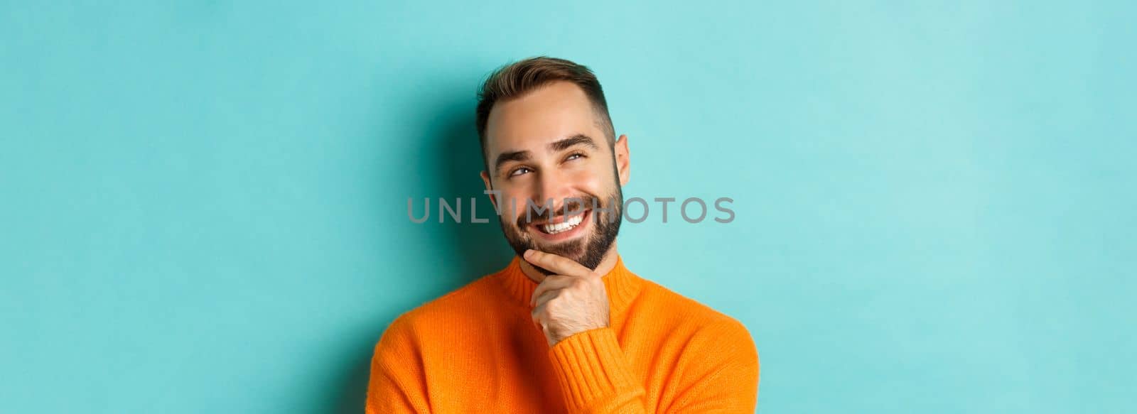 Close-up of caucasian male model having an idea, smiling and looking upper left corner thoughtful, imaging plan, standing over light blue background.