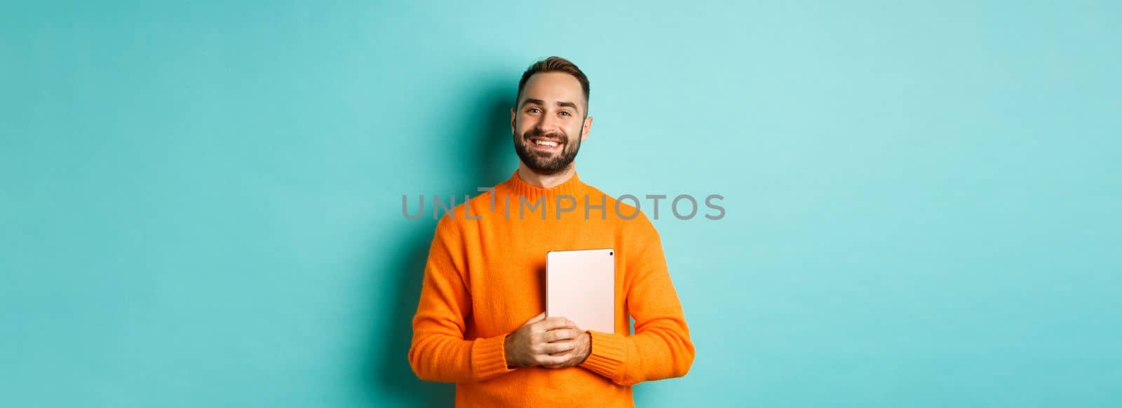 Handsome freelancer man holding laptop and smiling, standing happy over light blue background.