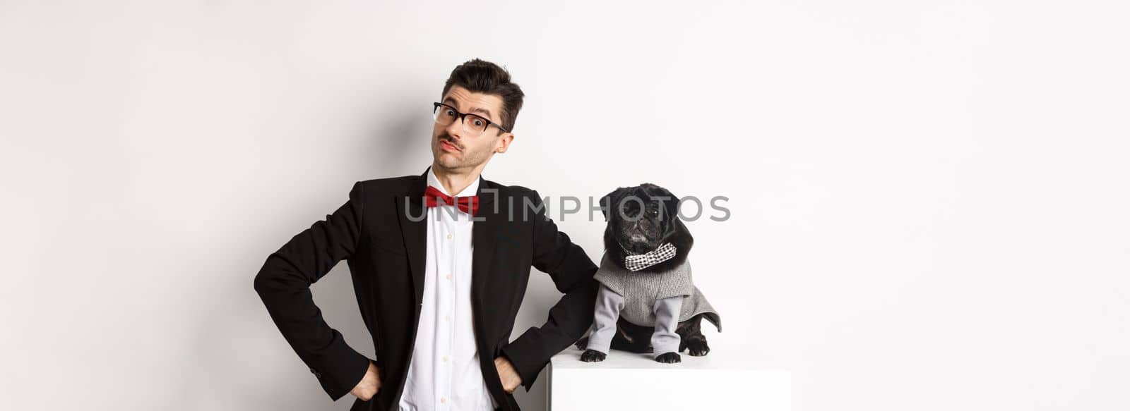 Animals, party and celebration concept. Handsome young man and puppy in formal suits looking at camera, standing over white background.