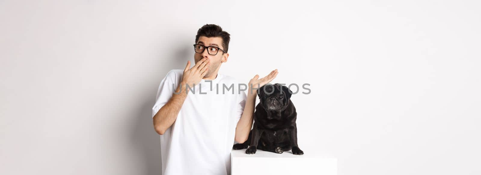 Surprised and shocked man in glasses, standing near cute black dog and staring right at logo, posing over white background.