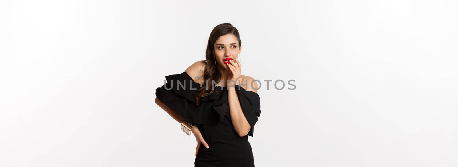 Fashion and beauty. Glamour woman in black dress thinking, having an idea, standing over white background.