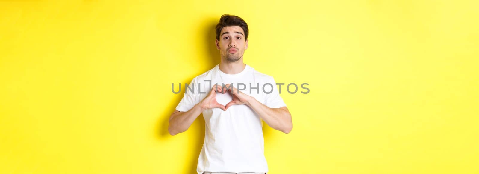 Cute guy pucker lips and waiting for kiss, showing heart gesture. Concept of love and romance by Benzoix