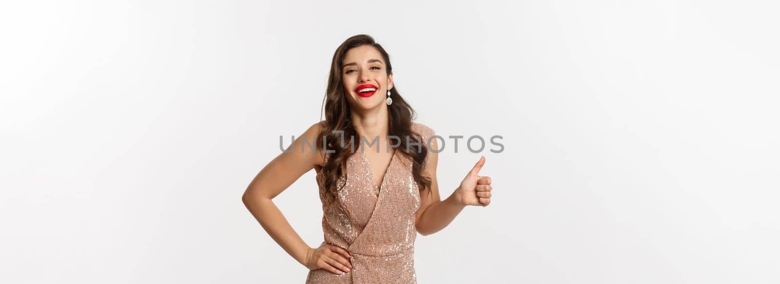 Concept of celebration, holidays and party. Happy elegant woman in evening dress with red lips, showing thumb up and laughing, approve and like something good by Benzoix