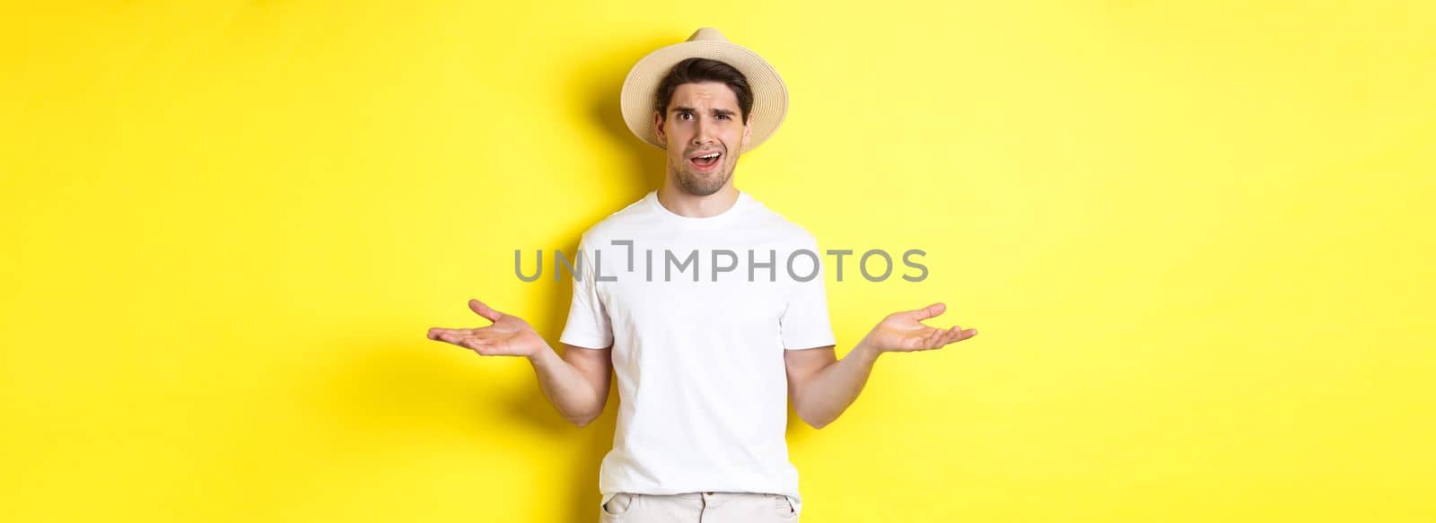 Concept of tourism and summer. Confused guy traveller shrugging, cant understand something, standing against yellow background.