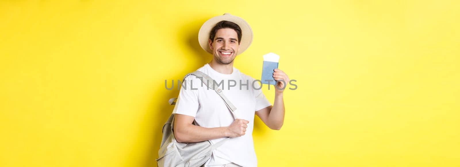 Tourism and vacation. Smiling young guy going on trip, holding backpack and showing passport with tickets, standing over yellow background by Benzoix