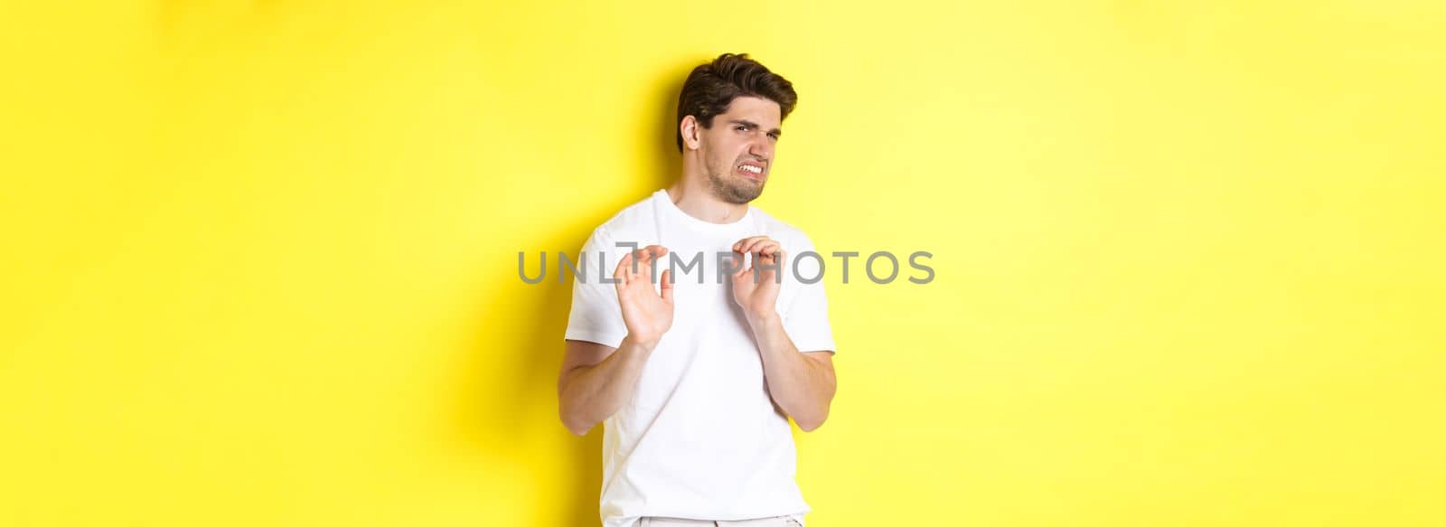 Digusted guy refusing and grimacing, looking at something with aversion, standing over yellow background. Copy space