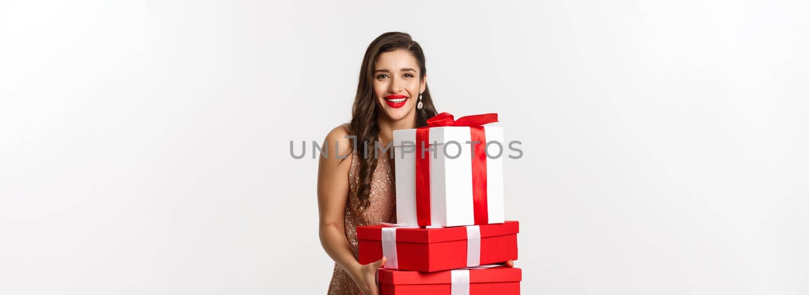 New Year, Christmas and celebration concept. Beautiful woman in party dress, holding gifts and presents, smiling happy, standing over white background.