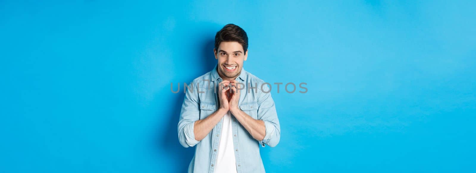 Funny cunning man having evil plan, scheming something and smiling devious, standing against blue background by Benzoix