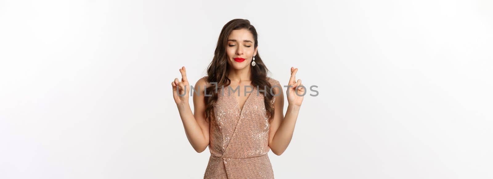 Concept of casino, celebration and party. Hopeful beautiful woman making a wish, cross fingers for good luck, dreaming of winning, white background.