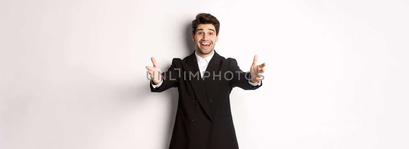 Portrait of happy attractive man in suit, hosting a party, reaching hands forward to greet you, want to hold something or hug, standing over white background by Benzoix