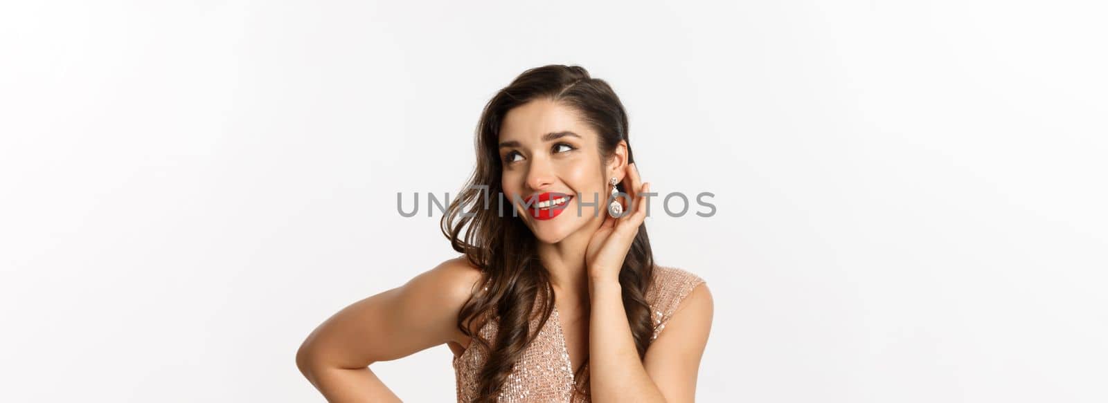 Concept of New Year celebration and winter holidays. Close up of beautiful woman dressed for party, blushing and smiling satisfied, showing her makeup, white background.