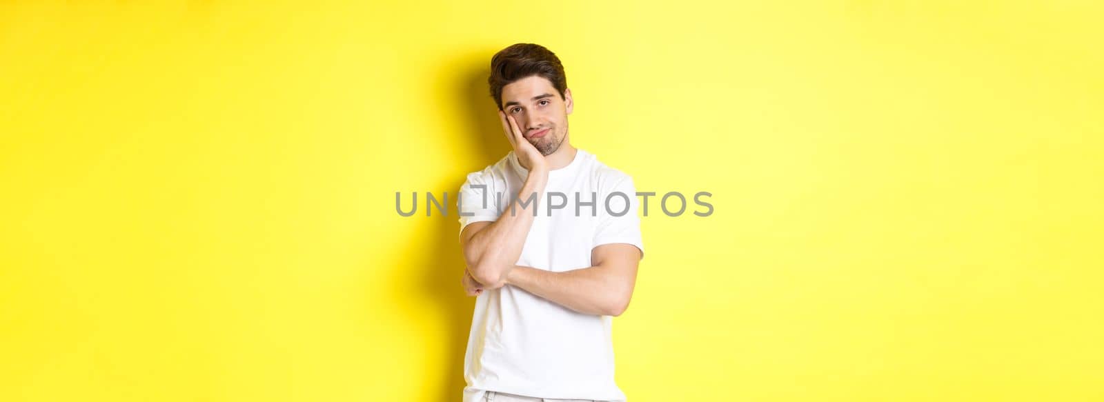 Bored and unamused man looking with indifference, standing in white clothes over yellow background by Benzoix