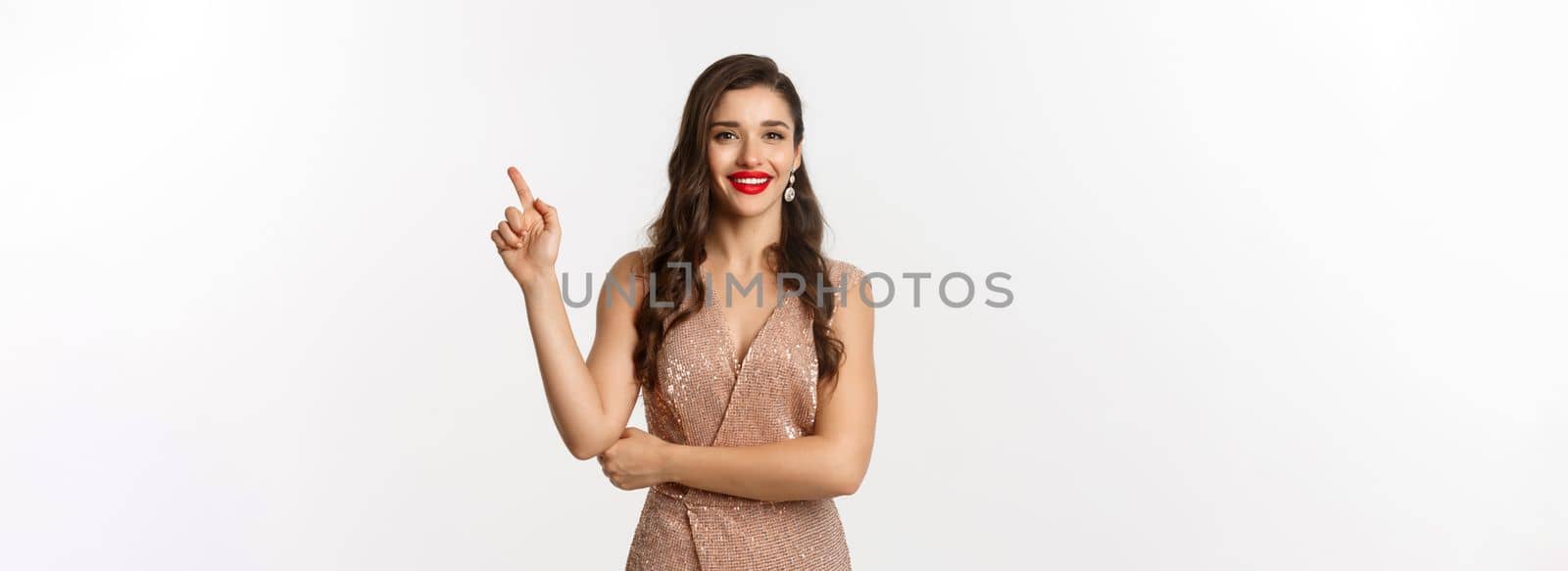 Beautiful woman in elegant dress on christmas party, pointing finger right at logo, smiling with red lips, standing over white background by Benzoix