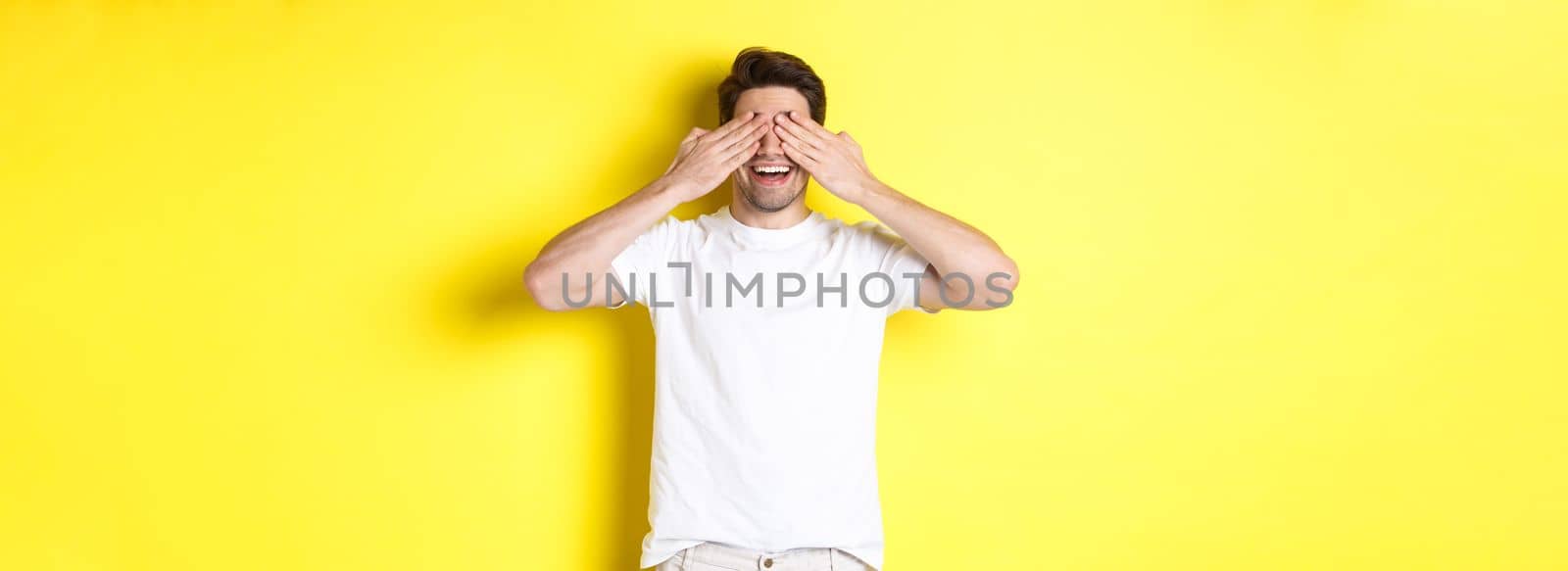 Happy man close eyes and waiting for surprise, smiling amused, standing over yellow background by Benzoix