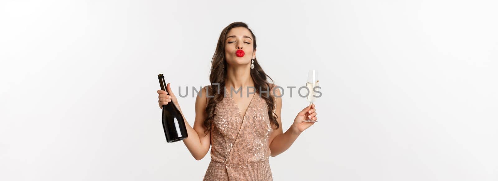 Winter holidays celebration concept. Beautiful and silly woman in elegant dress enjoying New Year party, drinking champagne, pucker lips for kiss, standing over white background.