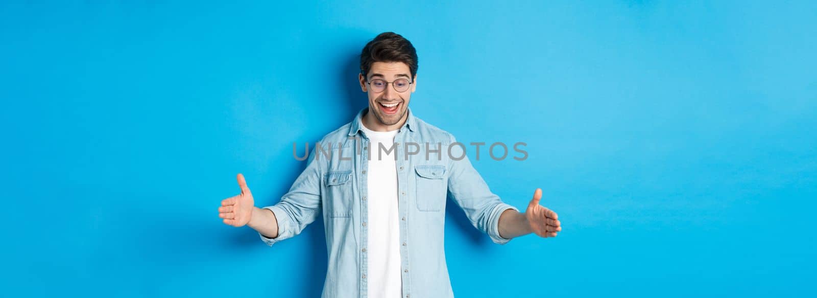 Excited handsome man showing big size object and looking amazed, standing over blue background.