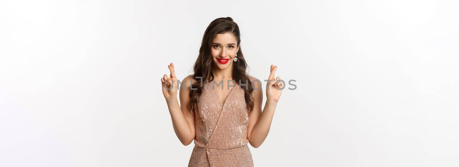Concept of casino, celebration and party. Hopeful beautiful woman making a wish, cross fingers for good luck and looking confident, white background.