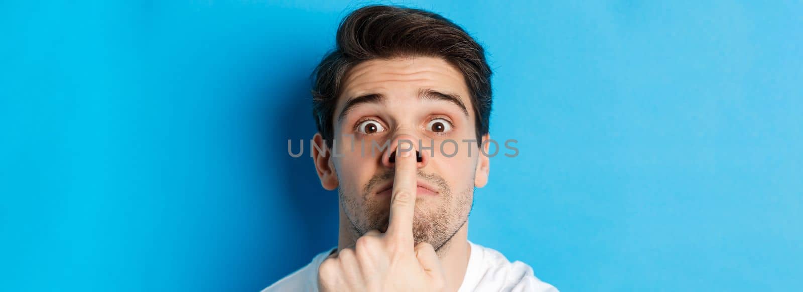Headshot of caucasian guy making funny expressions, standing over blue background.