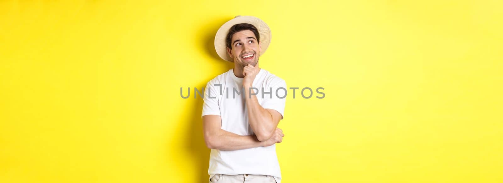 Young thoughtful man tourist imaging something, looking at upper left corner and smiling, thinking and standing over yellow background.