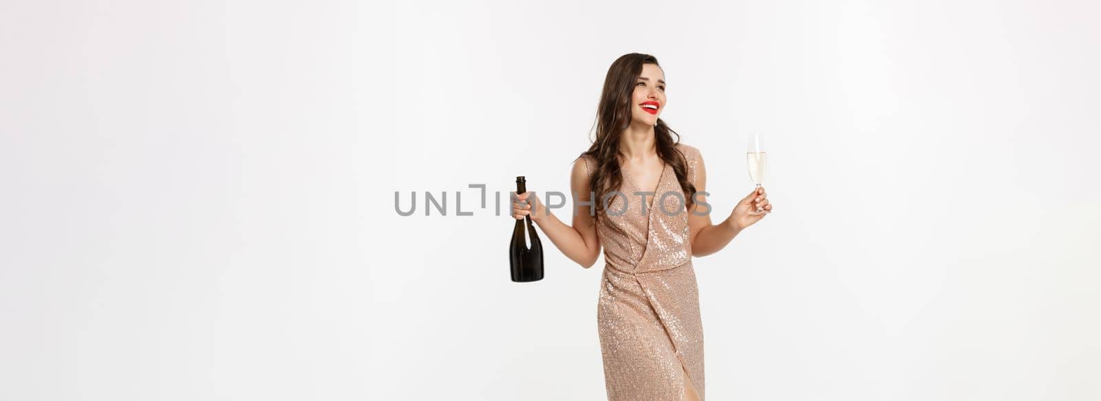 Christmas party and celebration concept. Full length of elegant woman with red lips, luxury dress, holding glass of champagne and bottle, white background by Benzoix