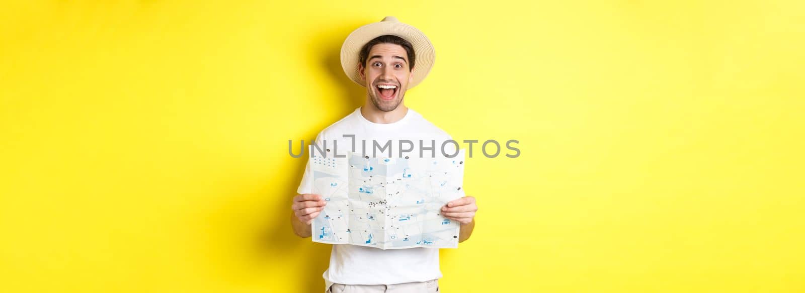 Travelling, vacation and tourism concept. Excited man tourist going sightseeing with map, standing over yellow background by Benzoix