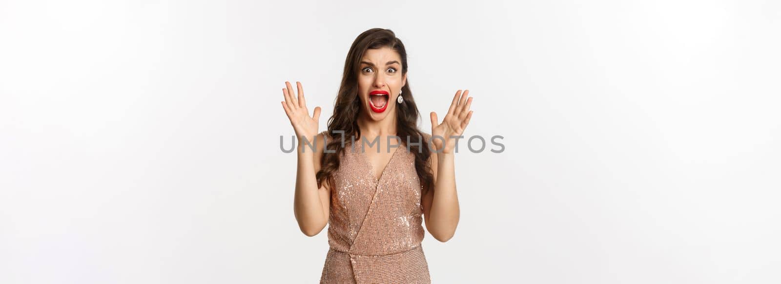 Celebration and party concept. Beautiful woman in elegant dress screaming and staring at camera scared, looking at something scary, standing over white background.