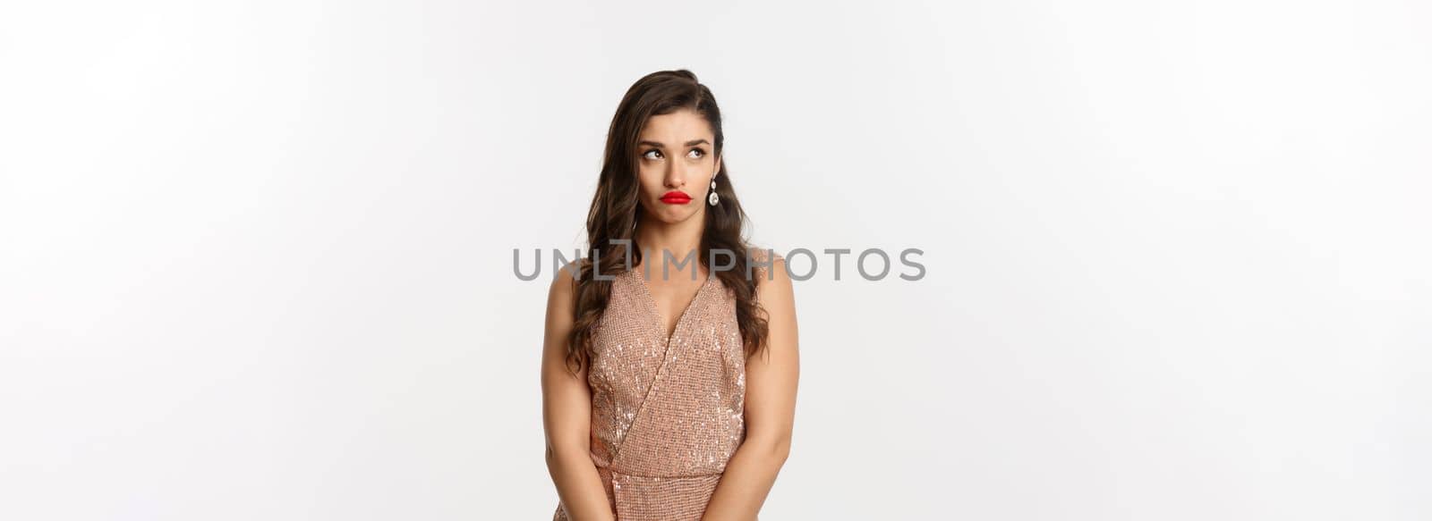 Celebration and party concept. Annoyed young woman losing temper, standing in glamour dress and looking away with bothered face, standing over white background.