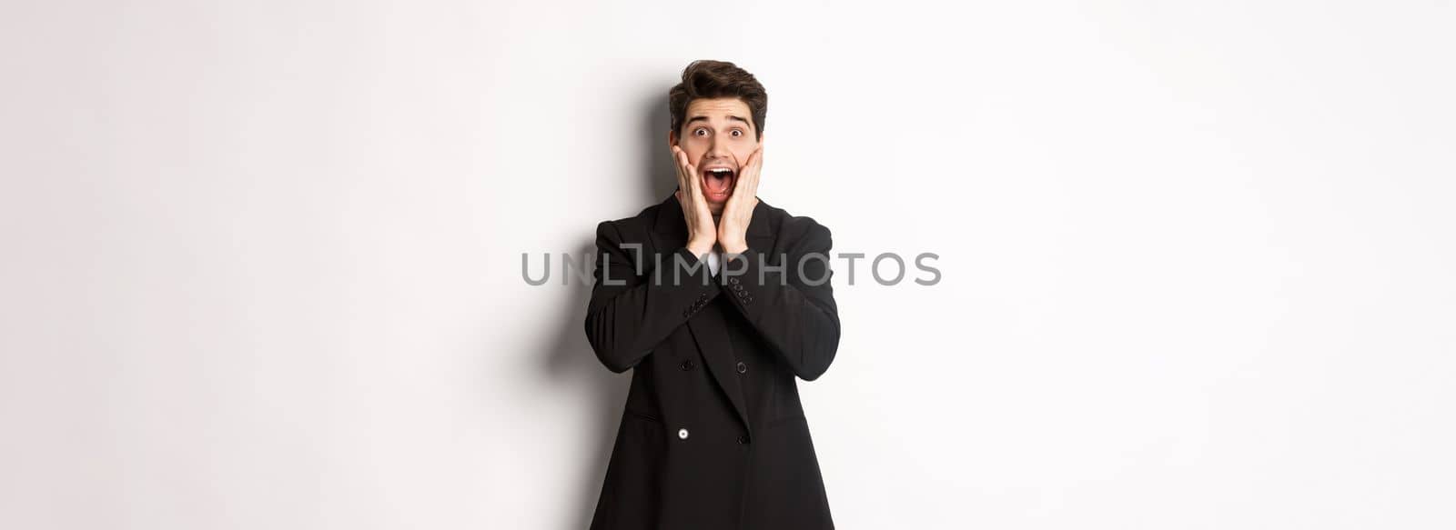 Portrait of surprised handsome businessman in suit, reacting to holidays promo, looking amazed at camera, standing over white background.