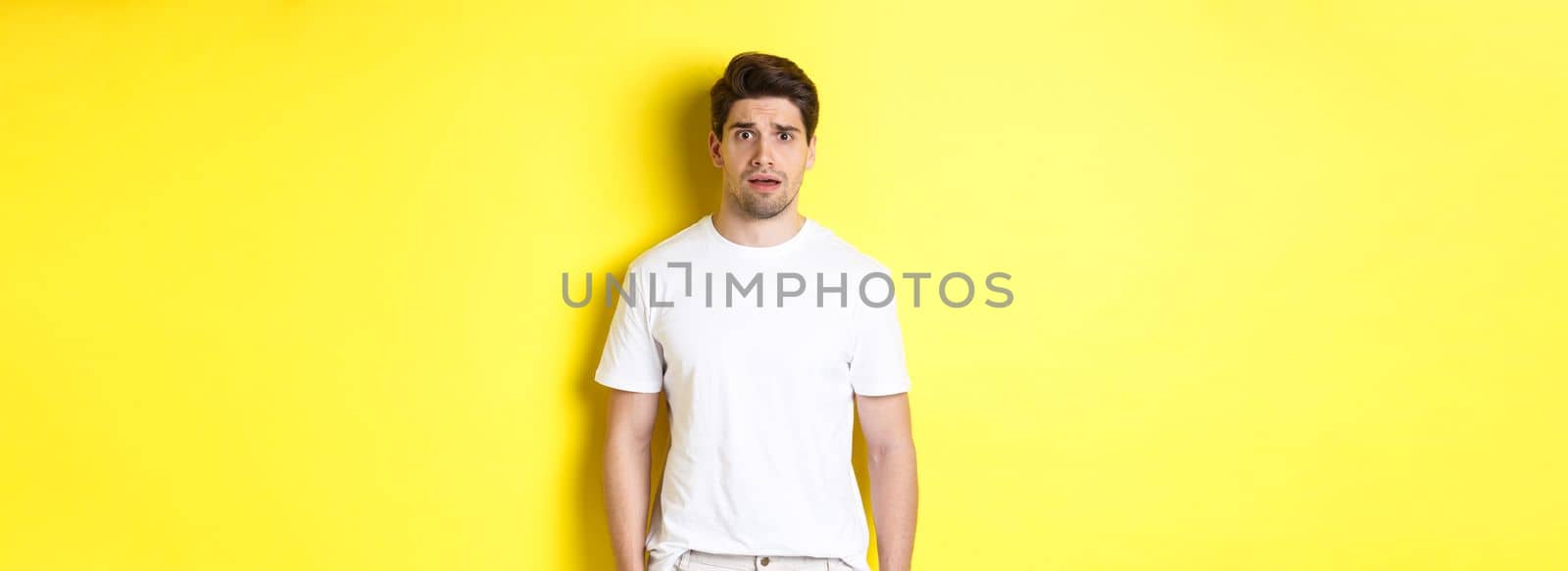 Image of confused and nervous man looking at something strange, frowning anxious, standing against yellow background.
