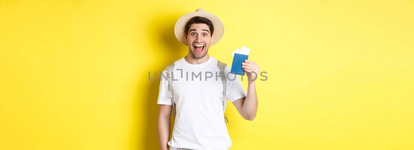 Tourism and vacation. Happy man tourist showing his passport with tickets, going on journey, standing over yellow background with backpack by Benzoix