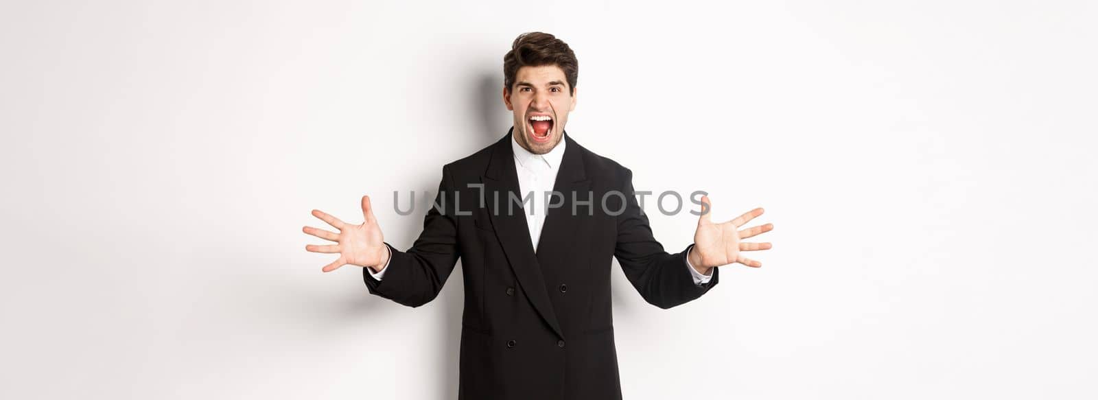 Portrait of pissed-off and frustrated businessman in suit, shouting angry and shaking hands, standing distressed against white background.