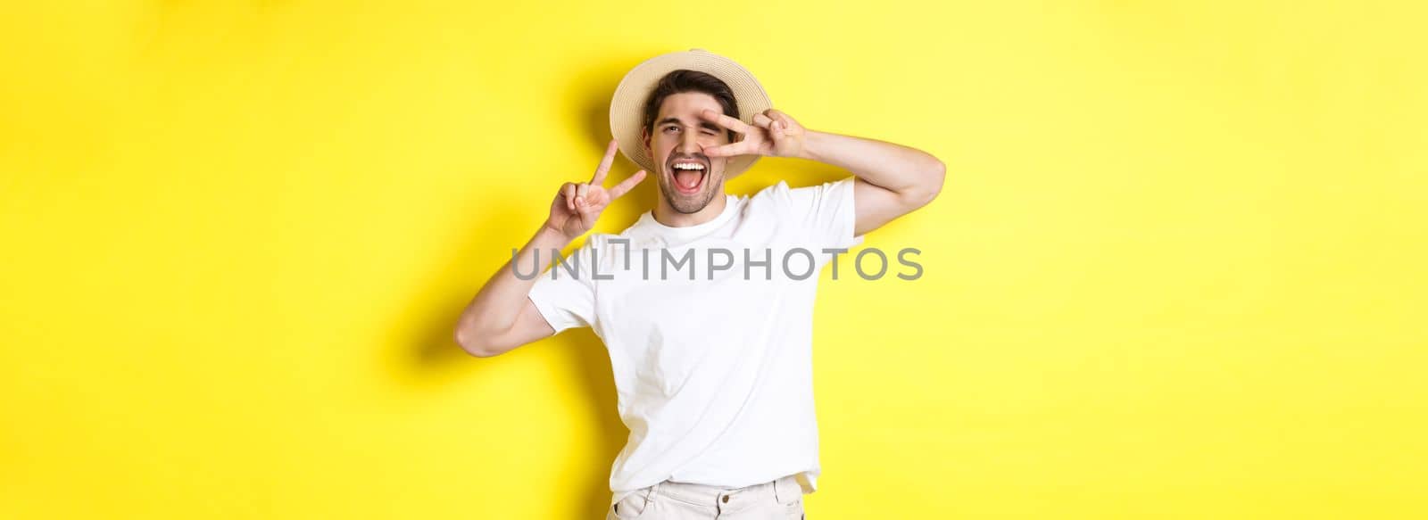 Concept of tourism and vacation. Happy man tourist posing for photo with peace signs, smiling excited, standing against yellow background by Benzoix