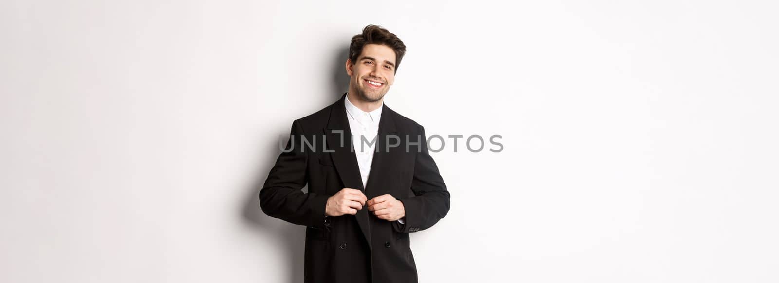 Image of handsome and confident businessman with beard, button down jacket and smiling, standing against white background.