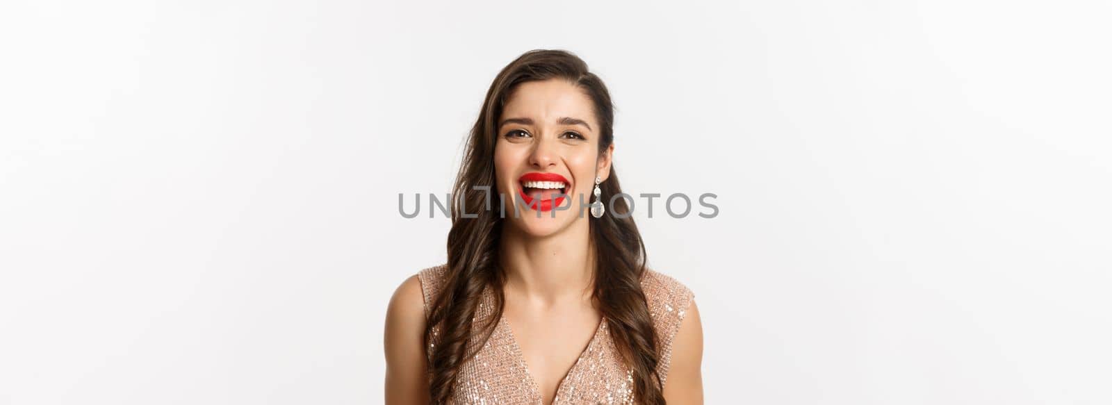 Concept of New Year celebration and winter holidays. Close-up of happy young woman dressed for party, laughing and smiling at camera, white background.