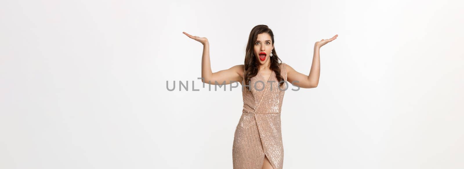 Party and celebration concept. Full-length of beautiful woman in elegant dress, standing near Christmas gifts and looking surprised, standing over white background.