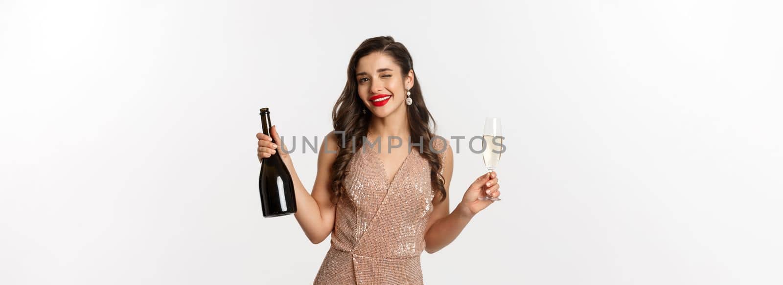 Winter holidays celebration concept. Beautiful woman enjoying Christmas and New Year party, drinking champagne and winking at camera, standing in elegant dress.