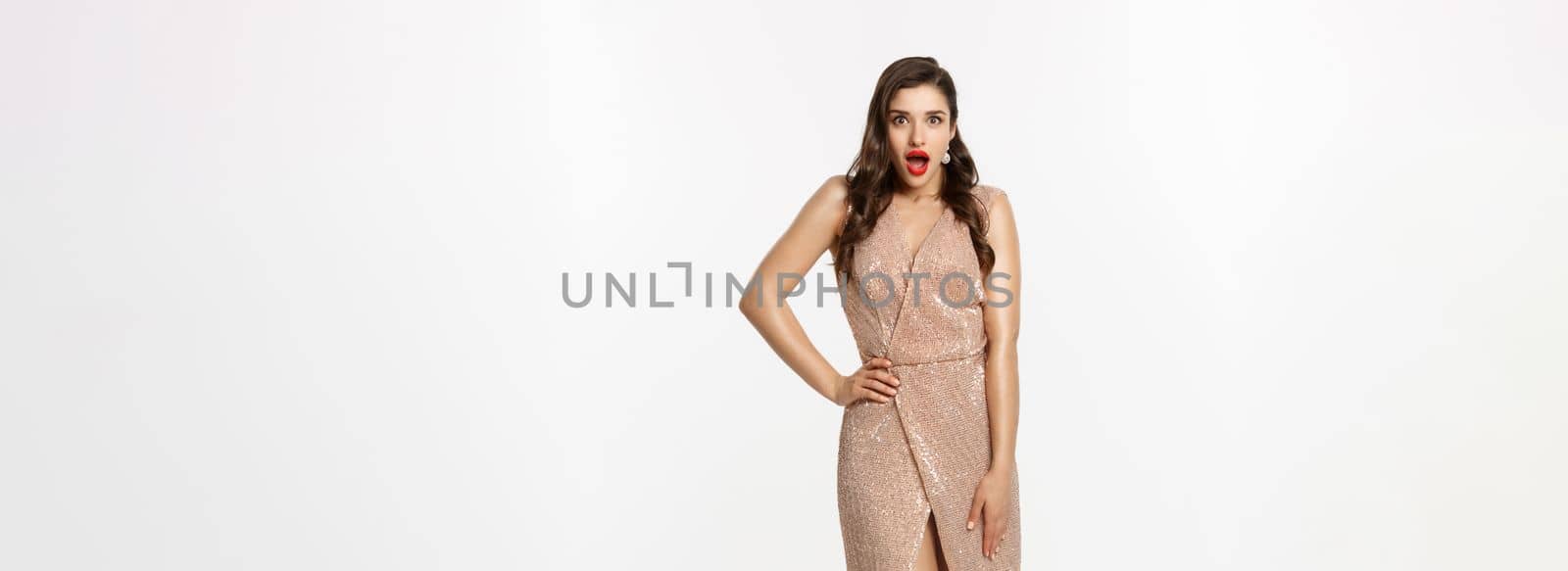 Christmas party and celebration concept. Full length of beautiful brunette woman looking surprised, wearing elegant dressed and gasping amazed at camera, white background by Benzoix