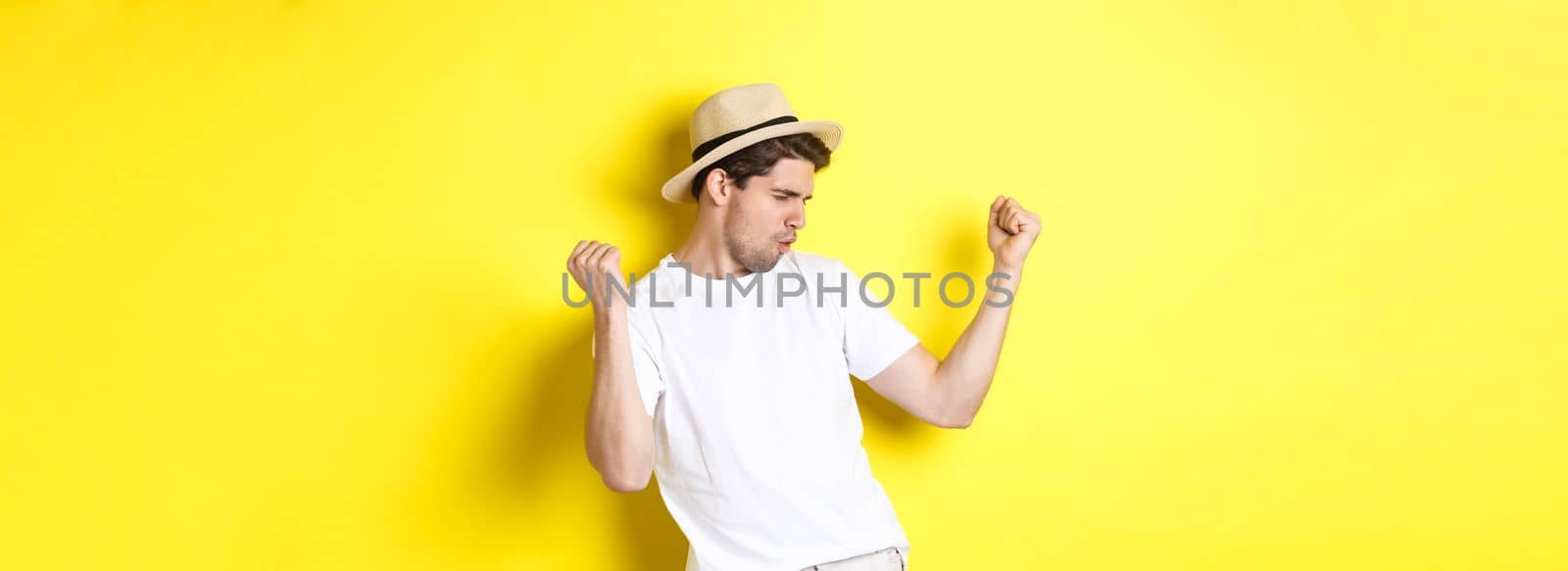 Concept of tourism and vacation. Lucky guy tourist rejoicing, making fist pump and saying yes, standing pleased against yellow background.