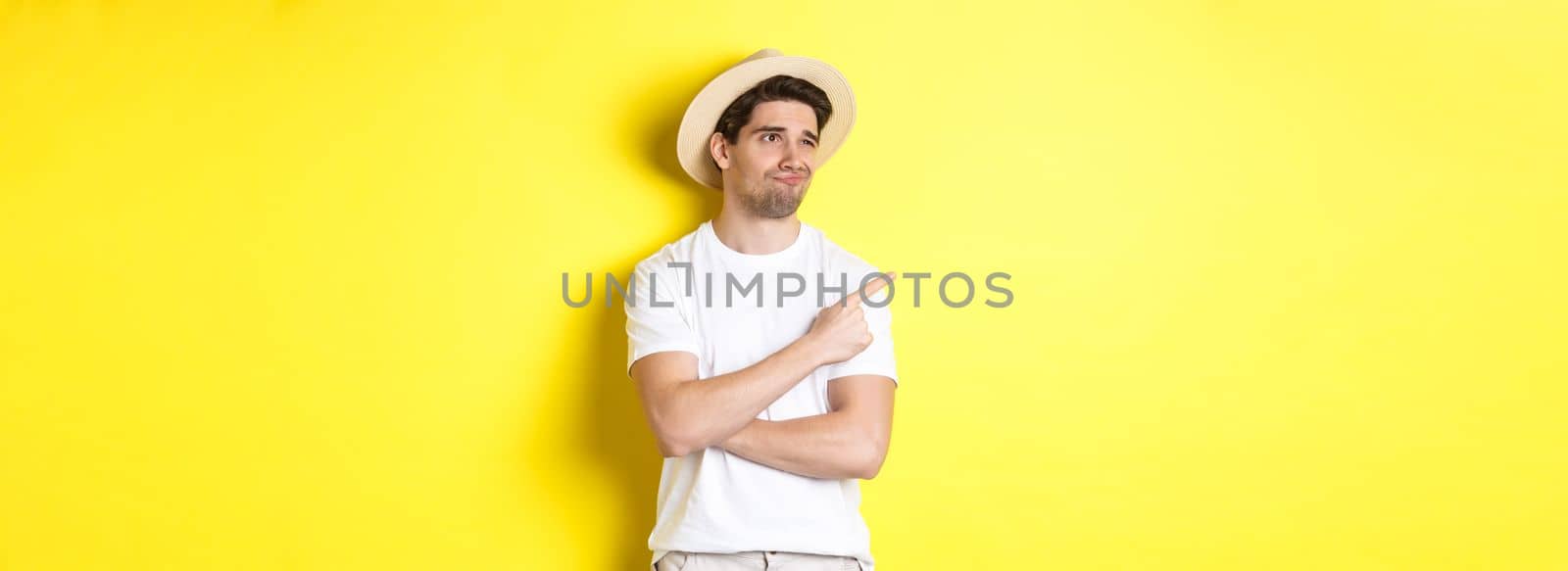Concept of tourism and lifestyle. Displeased male tourist complaining, looking and pointing finger at upper left corner promo with disappointment, standing against yellow background.