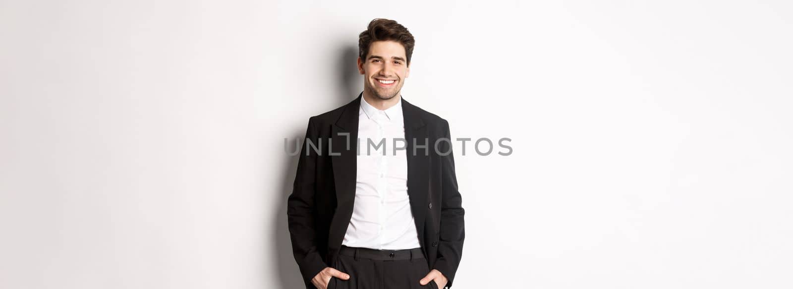 Image of handsome caucasian man in party suit, smiling pleased, attend formal event, standing over white background.